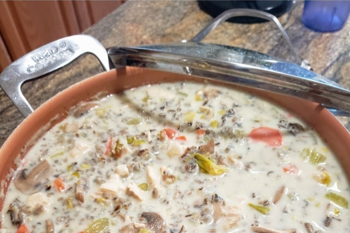 Pot of creamy chicken wild rice soup with chicken, carrots, celery, and mushrooms