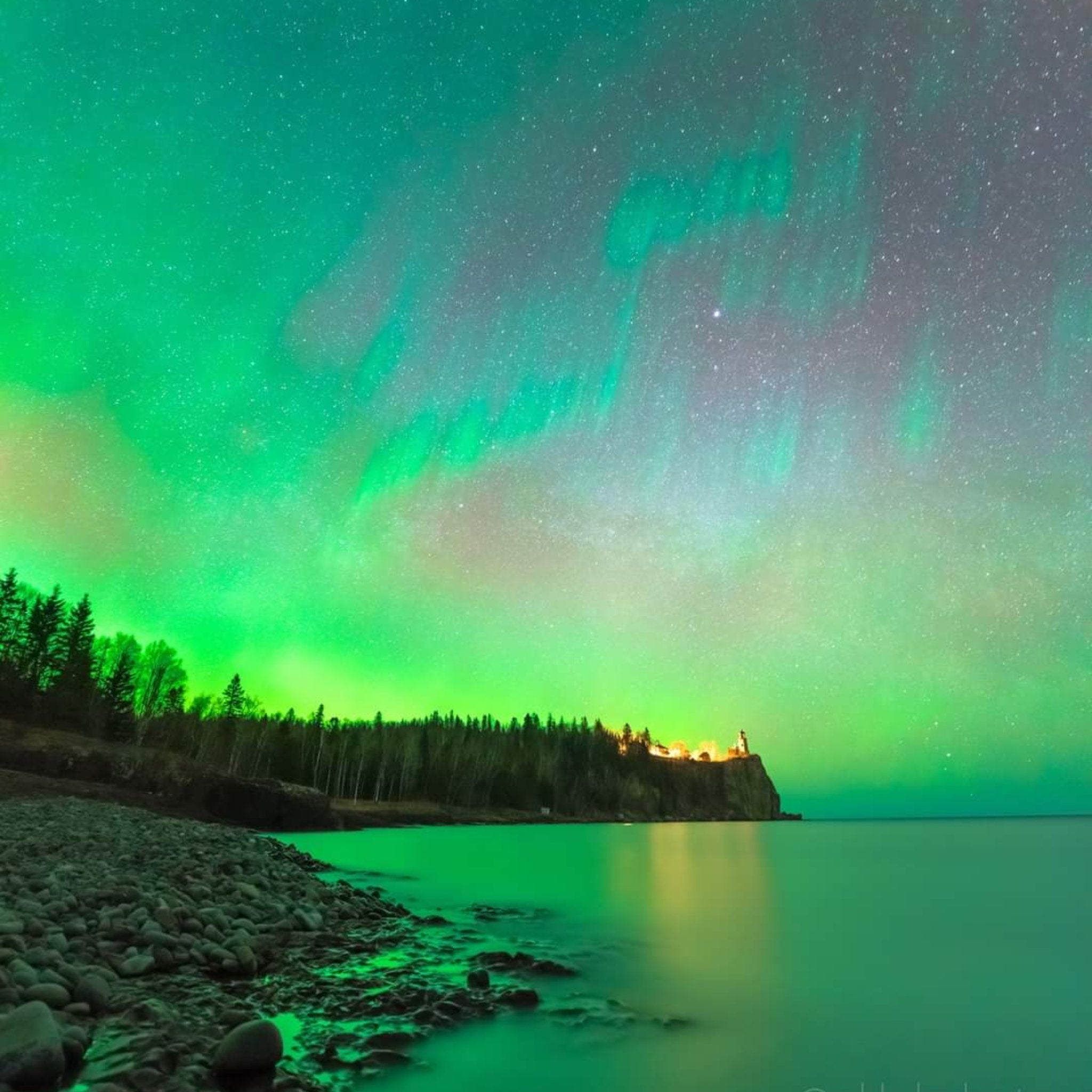 Aurora borealis over a lake with trees and a lighthouse in the background